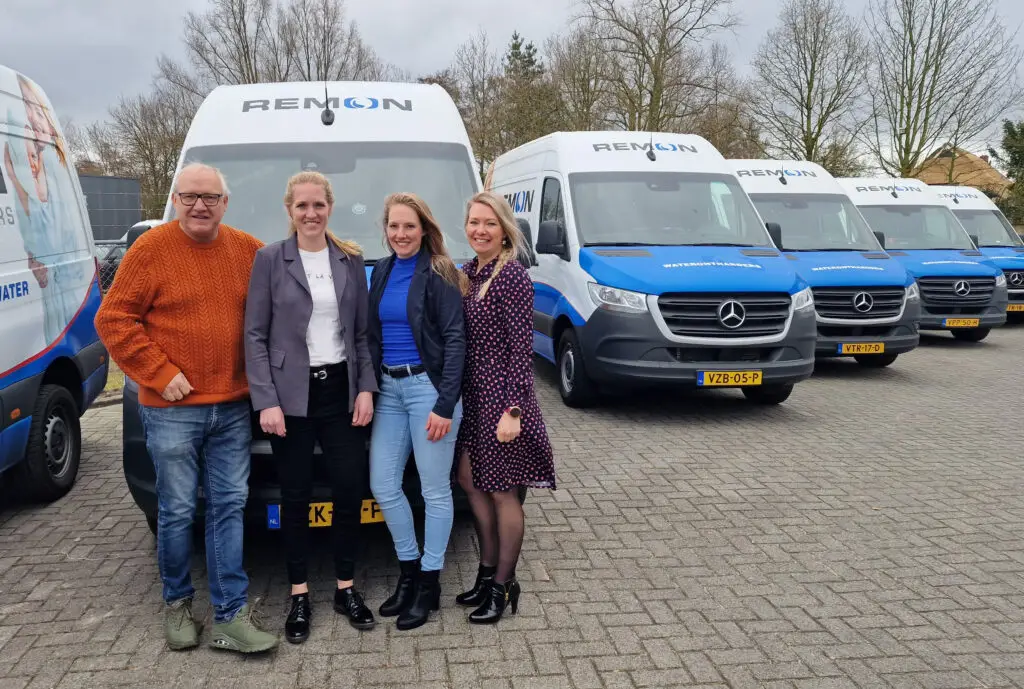Vier medewerkers van Remon Waterontharders poseren voor bedrijfsbussen met logo, symbool voor verschillende generaties binnen het familiebedrijf.